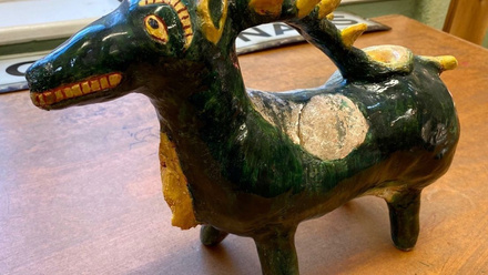 A green reconstructed medieval aquamanile, which looks something like a deer with antlers that go as far back as its lower back.