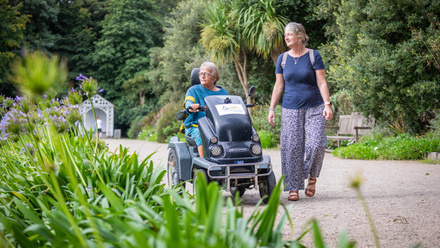 Two women on a garden path, one in an all terrain wheelchair.
