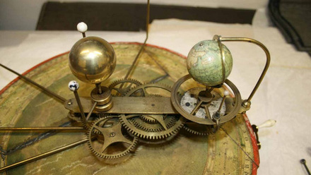 A Mechanical model showing a model of the earth that with gogs, will turn around a centre golden orb (sun) representing the earths rotation.