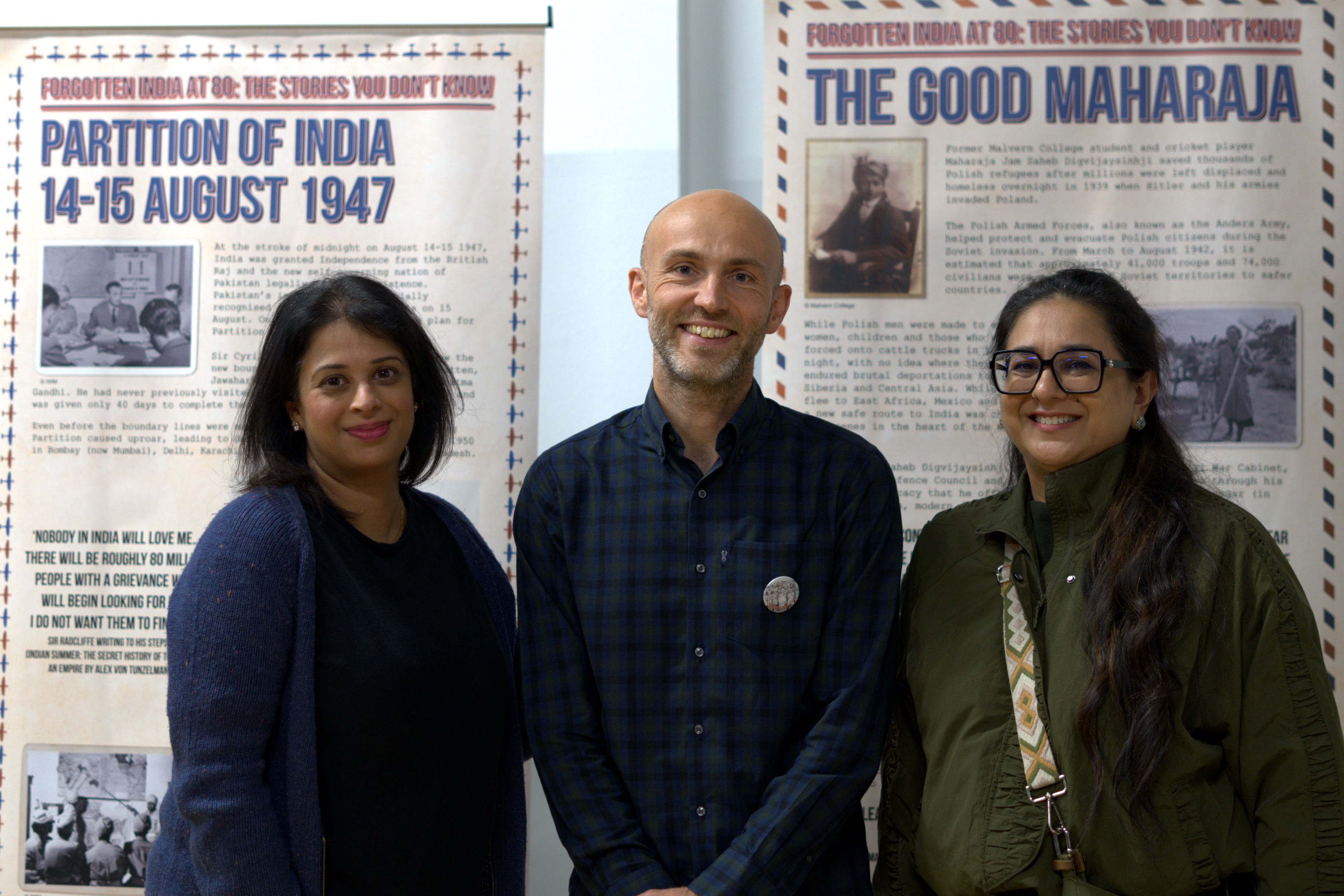 Three people stood in front of two pop up banners covered in text and some small images.