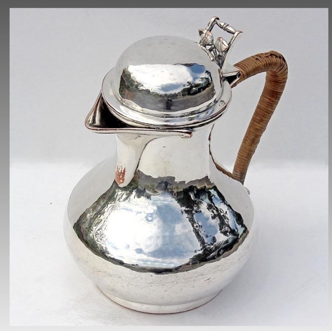 A hammered silver jug, with a lid that can flip up. The handle appears to have woven material around it so it can be lifted even when the jug is hot.