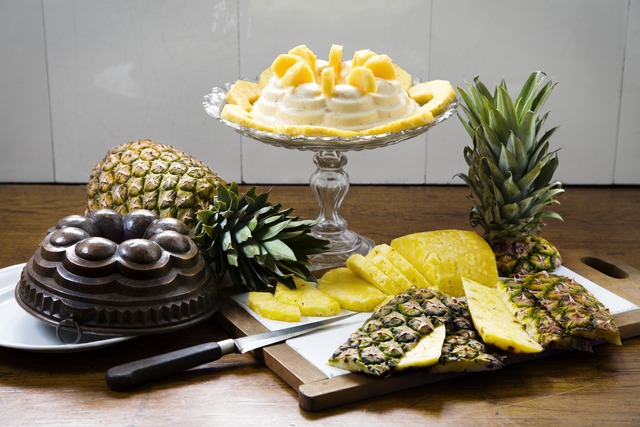 Historical display of prepared pineapples, including mousse on a standing glass dish and slices on a wooden board.