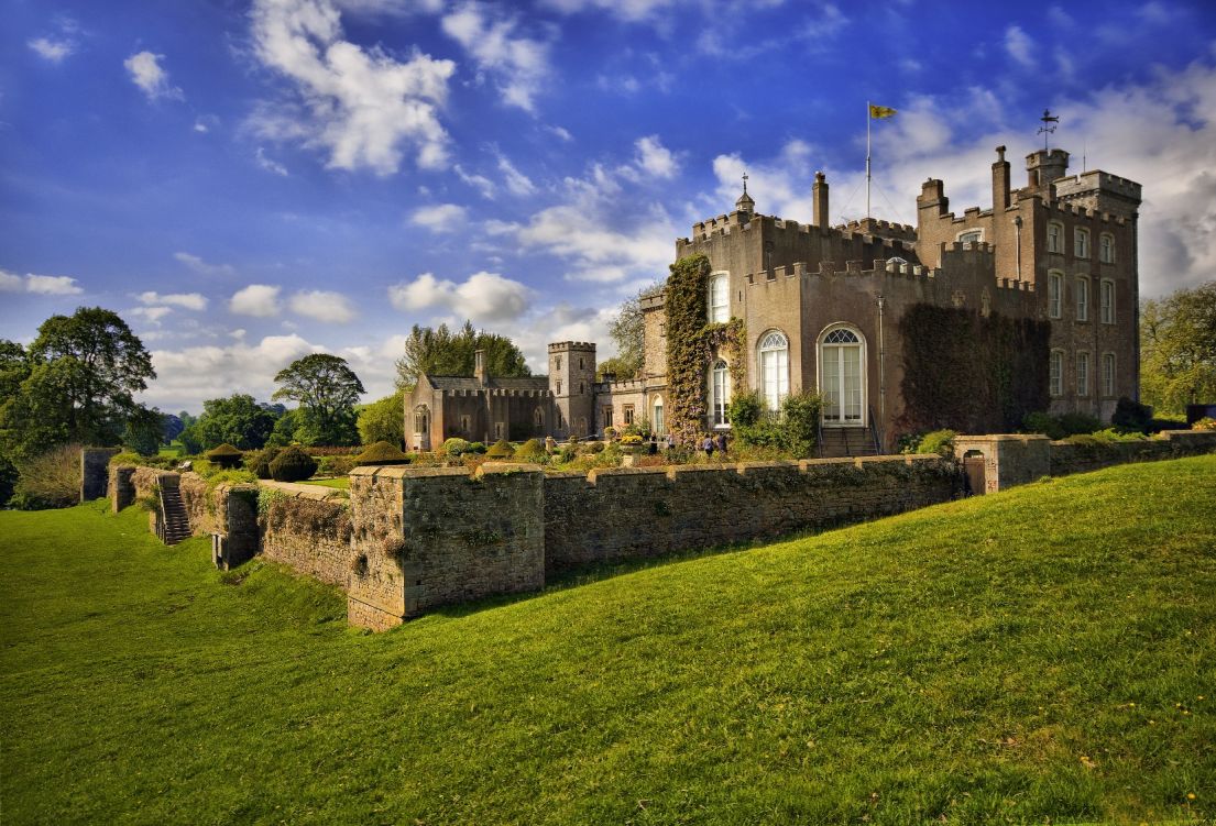 A photo taken from the lawn of a grand stone castle of yellowish brown stone.