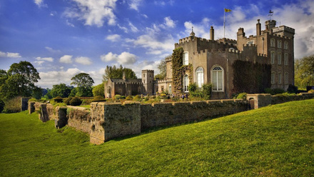 A photo taken from the lawn of a grand stone castle of yellowish brown stone.