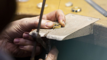 A close up of a gold ring on a wooden wedge. It is being cut with a wire on a saw.