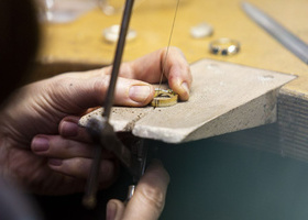 A close up of a gold ring on a wooden wedge. It is being cut with a wire on a saw.