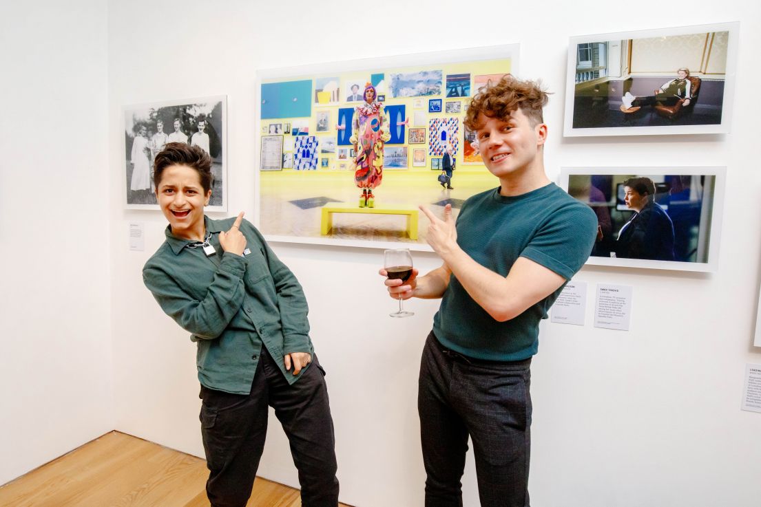 Two individuals standing in-front of art and playfully pointing back to highlight the person in the art behind them.