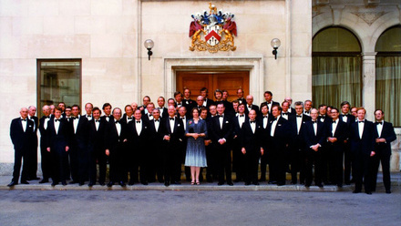 A staff photograph taken outside of a building, with men in suites and the sole female partner at Herbert Smith Freehills stood at the front in blue.
