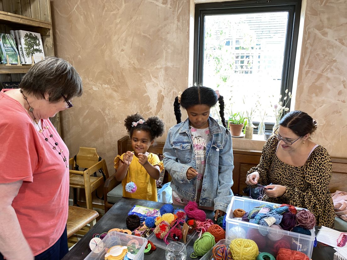 Two children and two women stand around a table with wool, threads and sewing tools.
