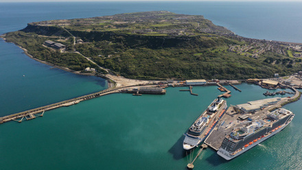 Aerial view of port with 2 large cruise liners in dock and  green hills rising in the distance.
