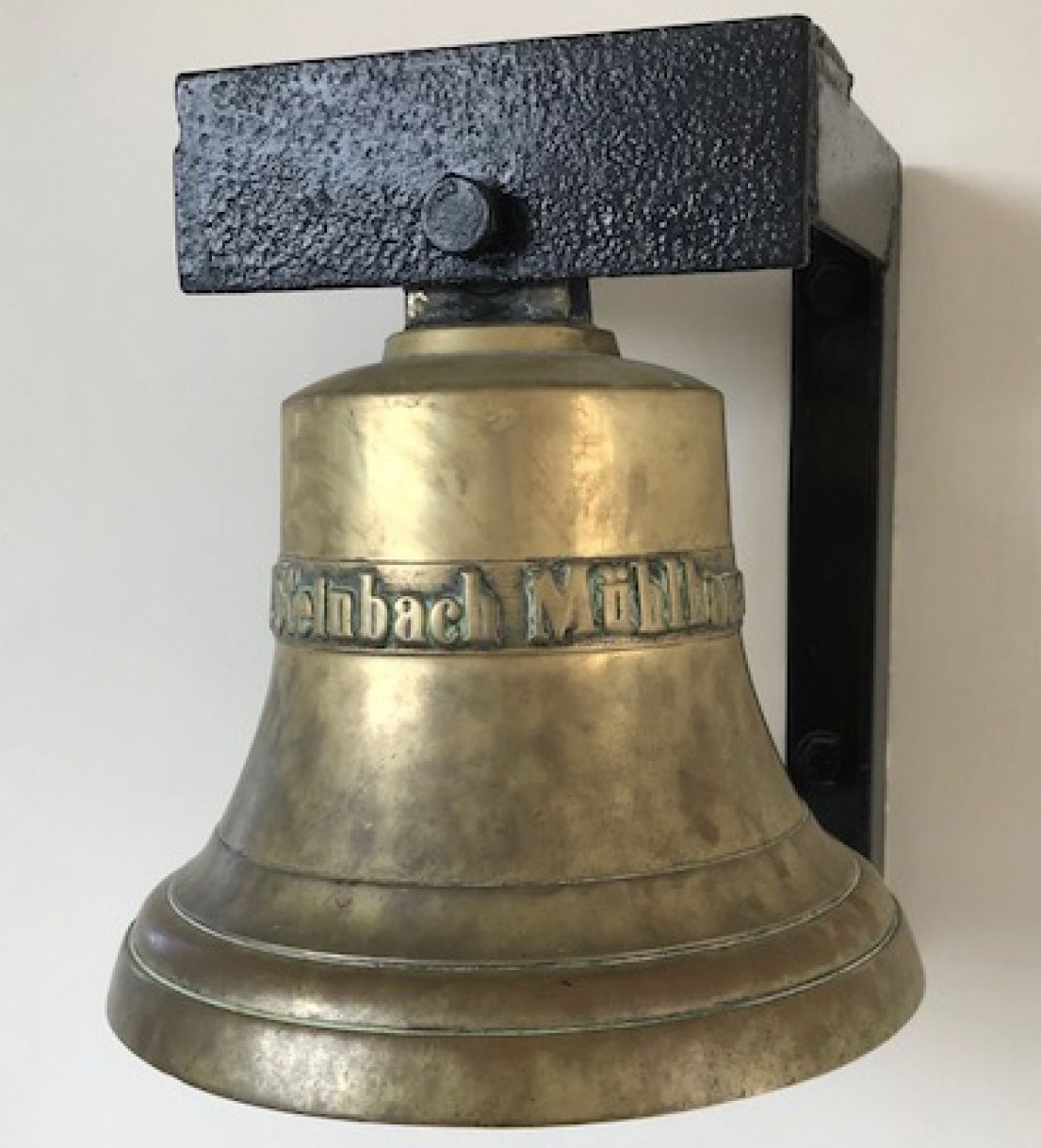 A brass bell mounted on the wall with some metal so it can still be rung.