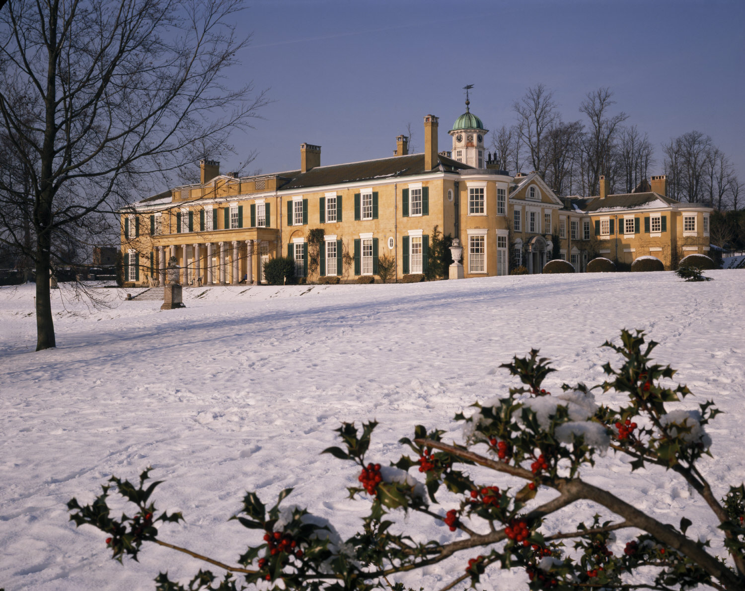 Large two-story brick building, with a clock tower, in a snow covered landscape.