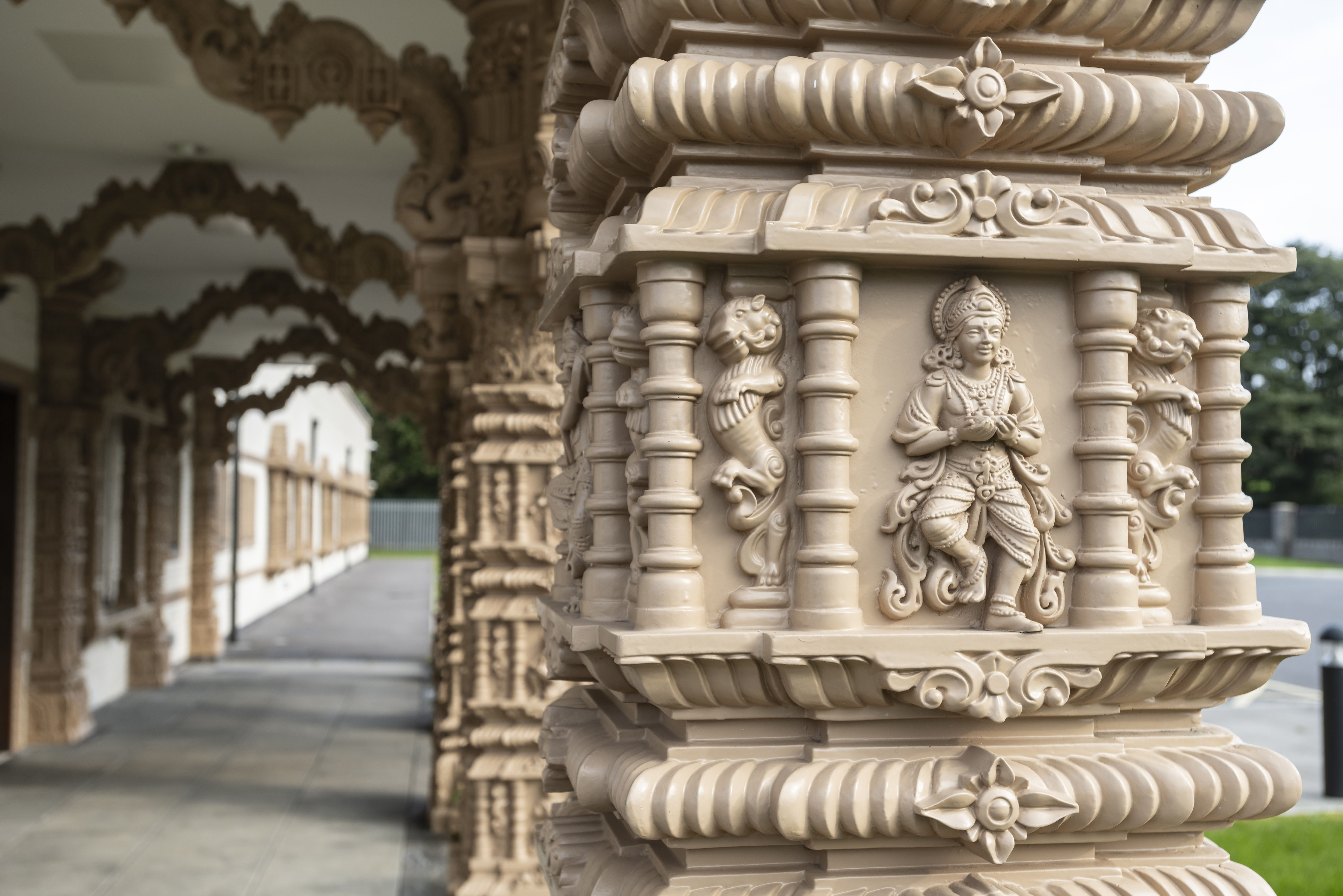 Close up of the decorative detail on a pillar in a colonnaded walkway. Showing a dancing figure, dragons? and flowers.