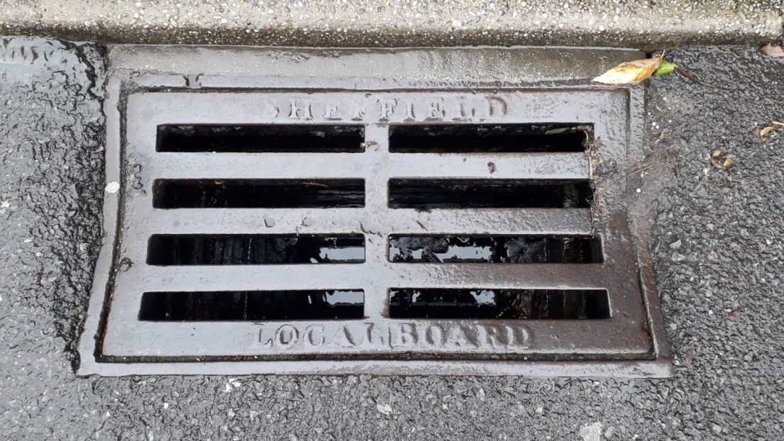 A metal drain, set in the side of a tarmacked road.