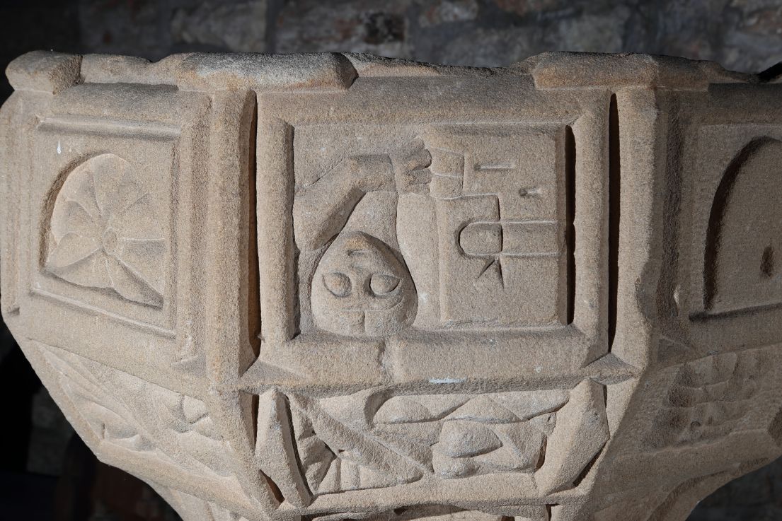 A stone font, which has various carvings decorating it on all sides.