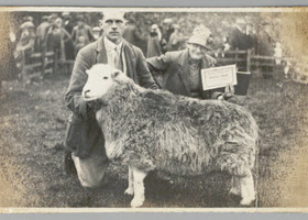 Man kneeling holding a sheep beside a woman holding a certificate.