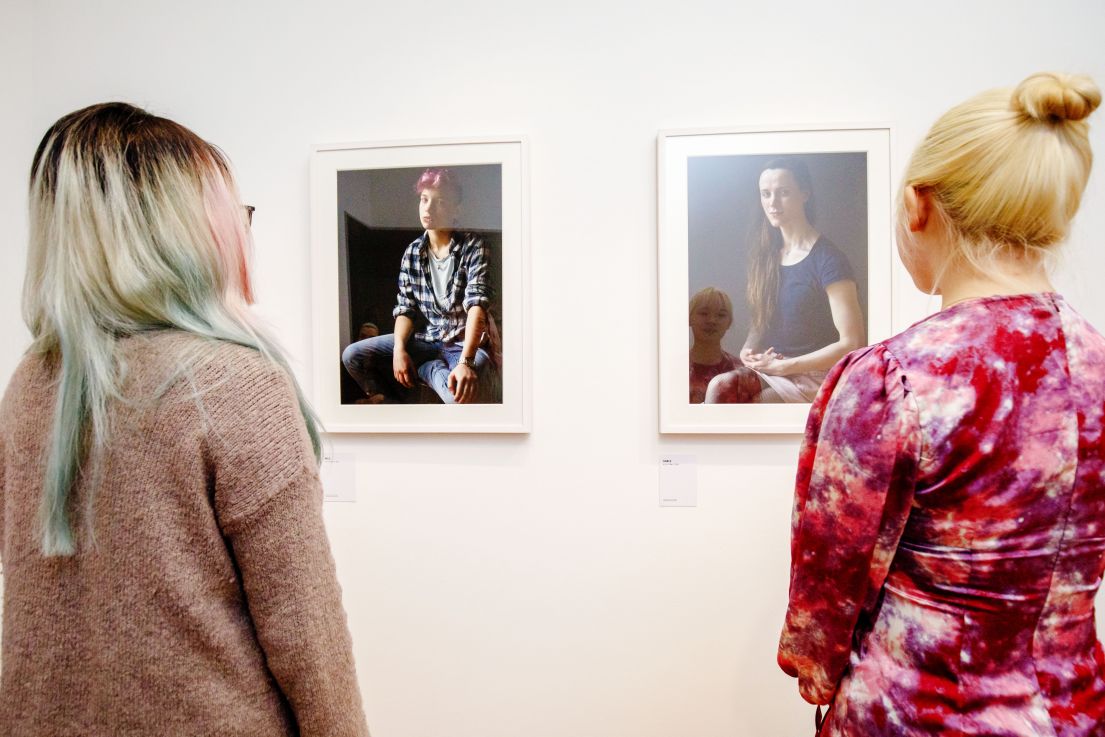 Two individuals admiring two pieces of photography on the wall of an exhibition.