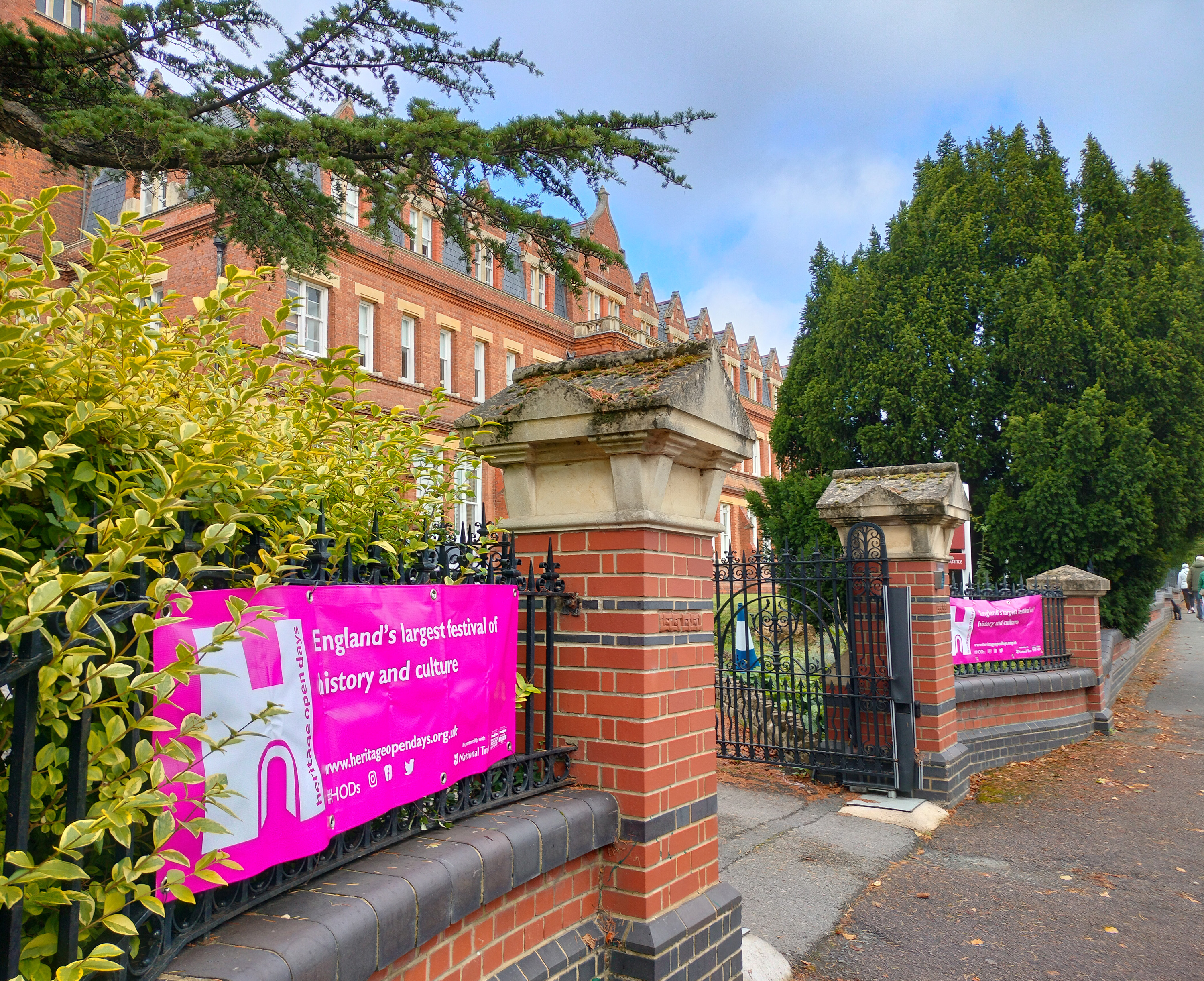 Pink banner stretched across railings at brick entrance gateway to a brick building.