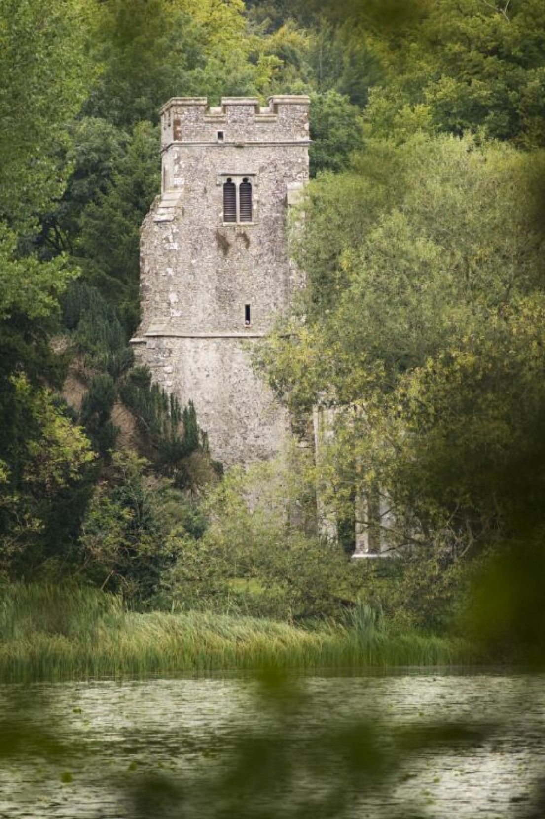From a distance, across a lake, a tall church tower appears out of thick trees.