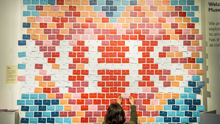 Wall of small rectangular coloured cards pinned into a display of a heart with the letters NHS across it.