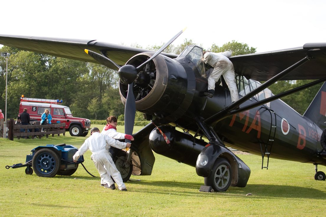 A dark Propeller plane being prepped for take off by three individuals in white overalls.