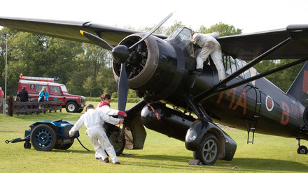 A dark Propeller plane being prepped for take off by three individuals in white overalls.