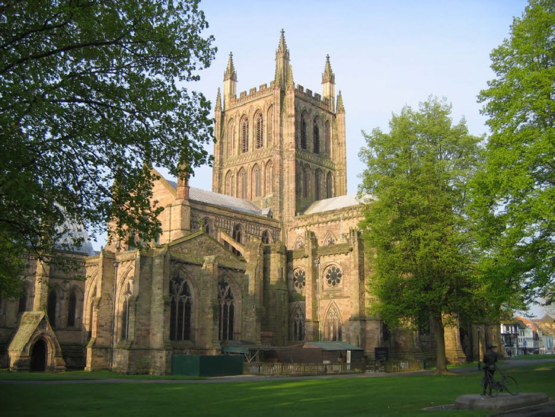 A light stone grand cathedral, with tall arched windows and centre tower visible between trees.