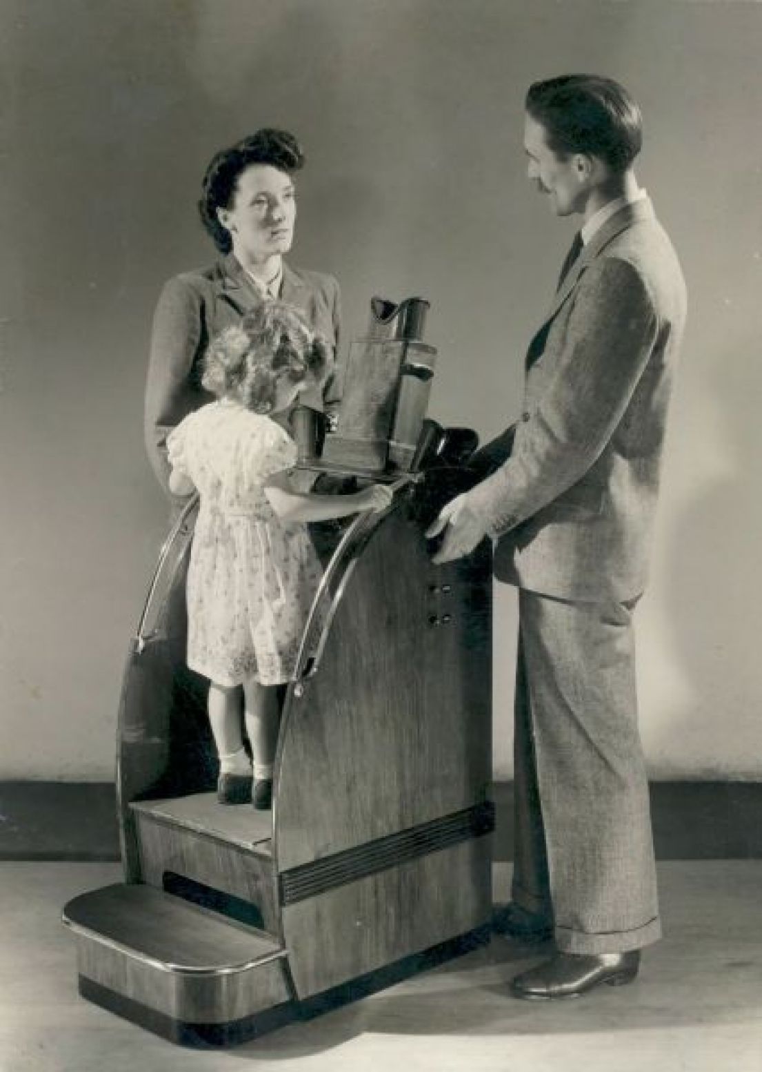 A small child stood on a portable x-ray machine on a small platform, which measures her feet. To each side of the x-ray are two adults.