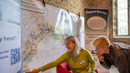 Two people pointing at a location on a large map hung on a wall.