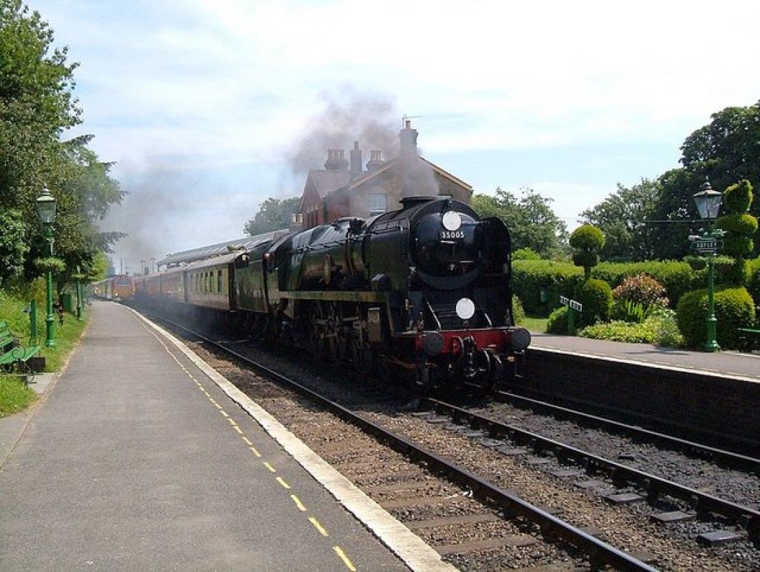 A steam locomotive train travelling through a station, the steam exiting the train from funnel.