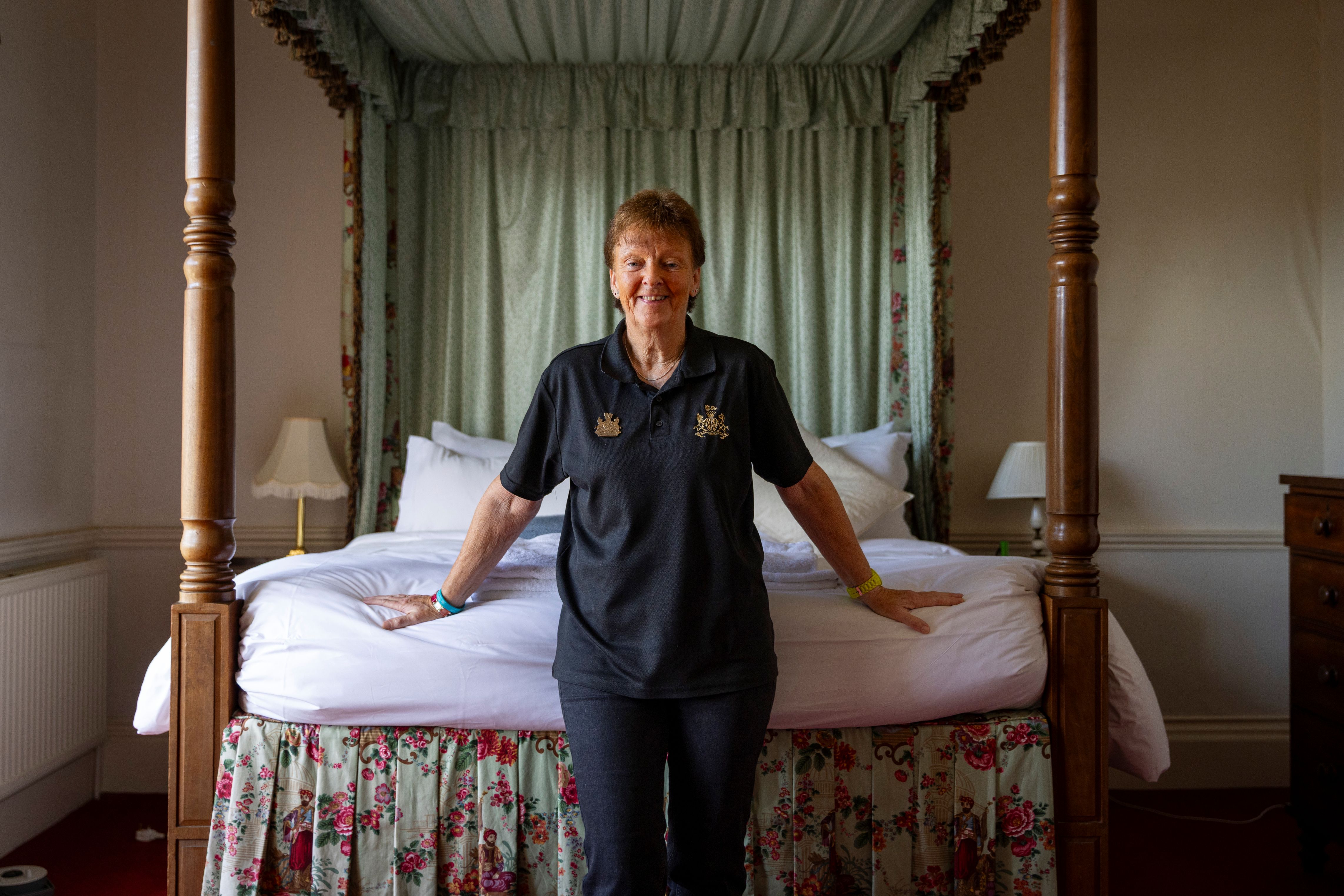 Woman in branded polo shirt uniform stood by four poster bed.