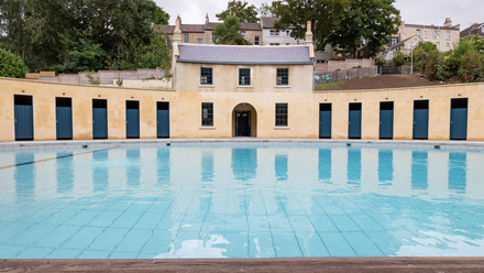 Two story building with single story wings arcing to each side round a blue pool.