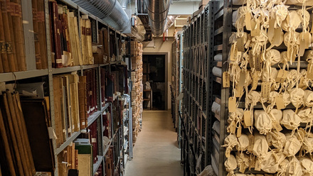 Metal shelving racks holding an assortment of boxes, old books and cloth wrapped bundles.