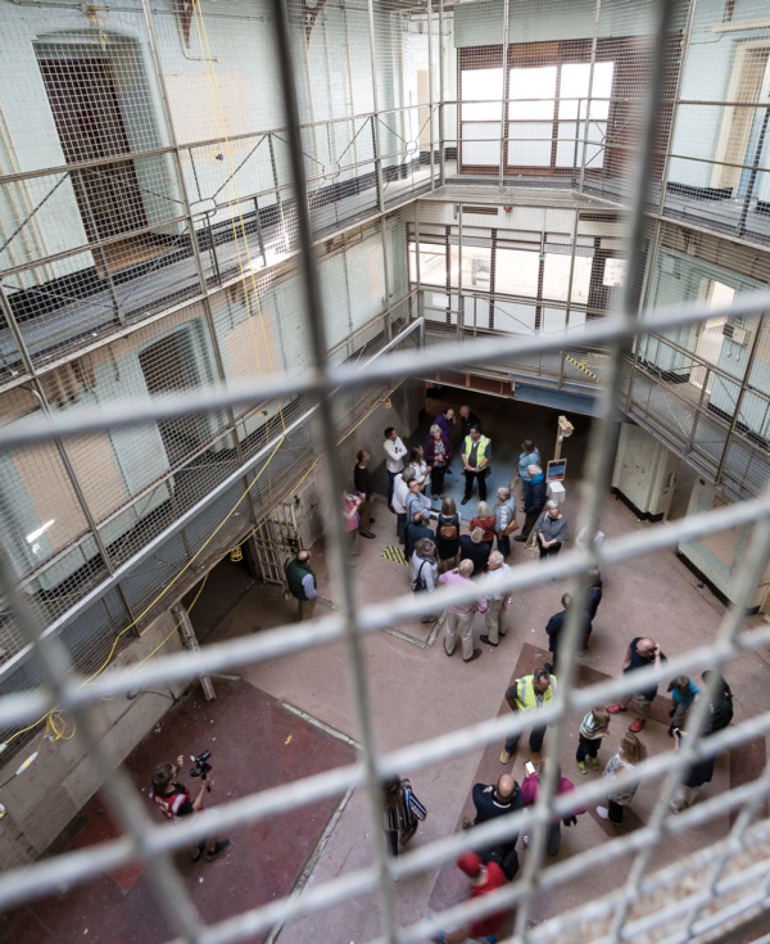 Looking down from a metal gridded balcony, you can see groups of people on tours in a three storied Victorian prison.