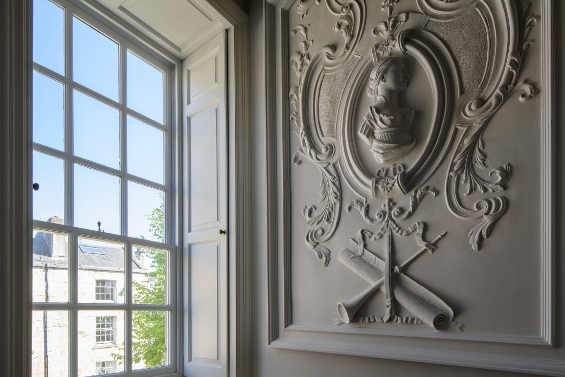 A decorated white panel next to a closed sash window.