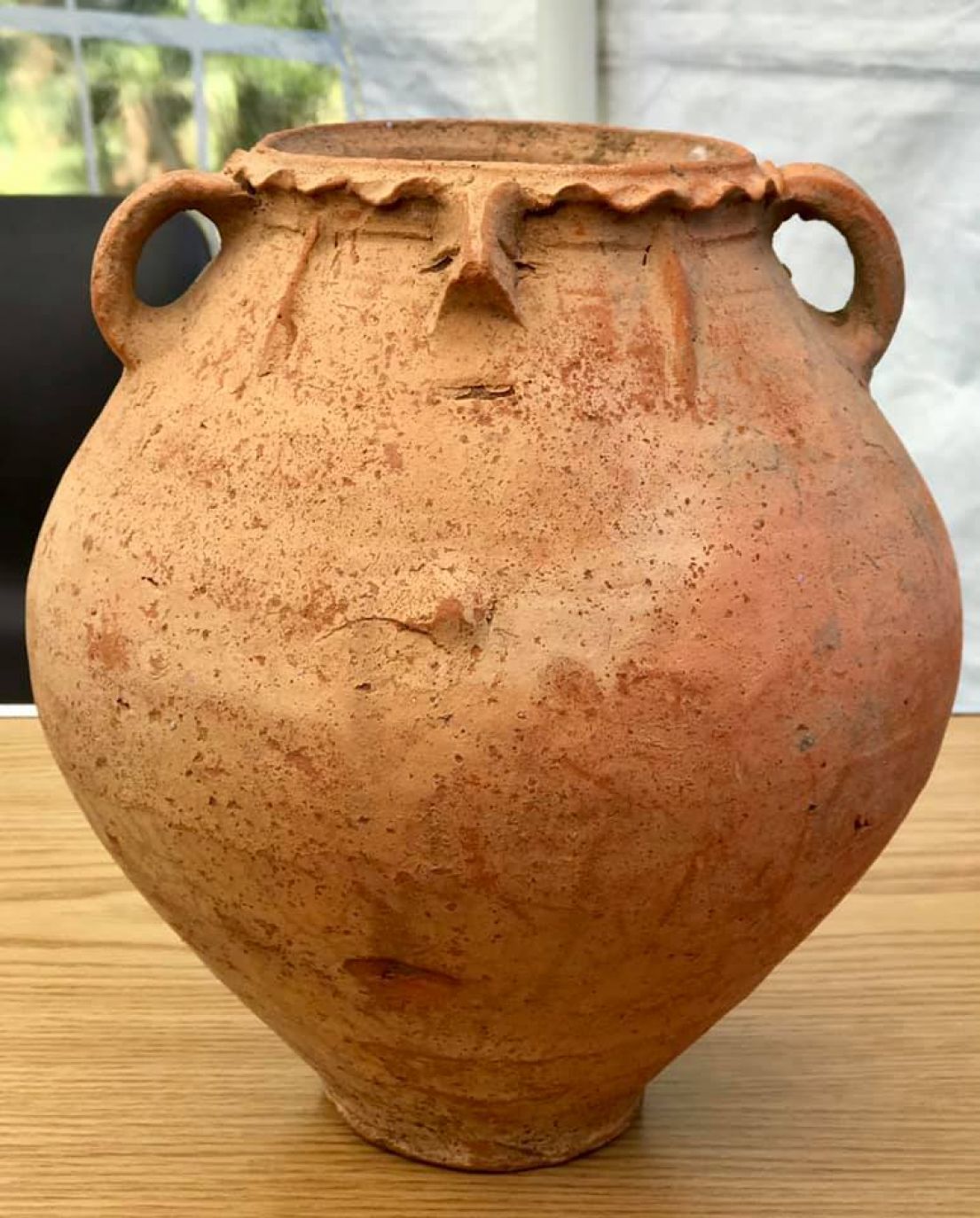 A reddish brown pot, with a decorated rim and two small handles at either side at the top.