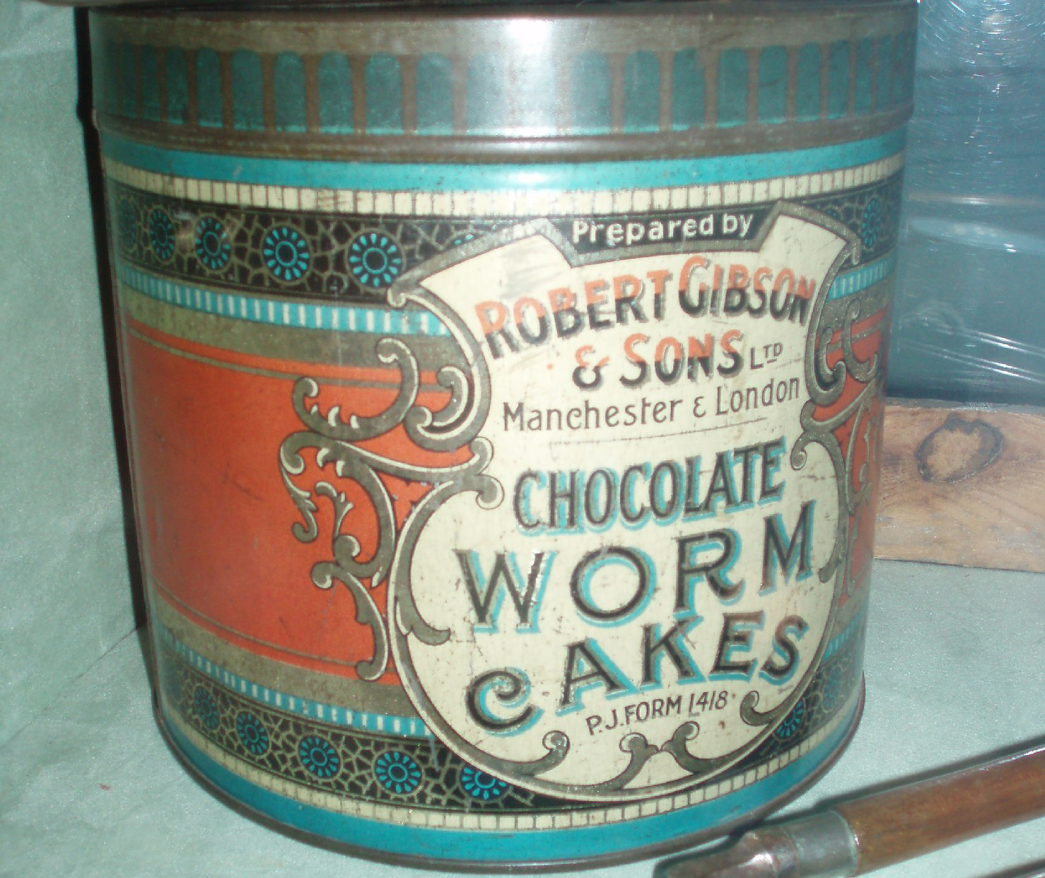 Squat, round metal tin with colourful old label advertising Chocolate Worm Cakes.
