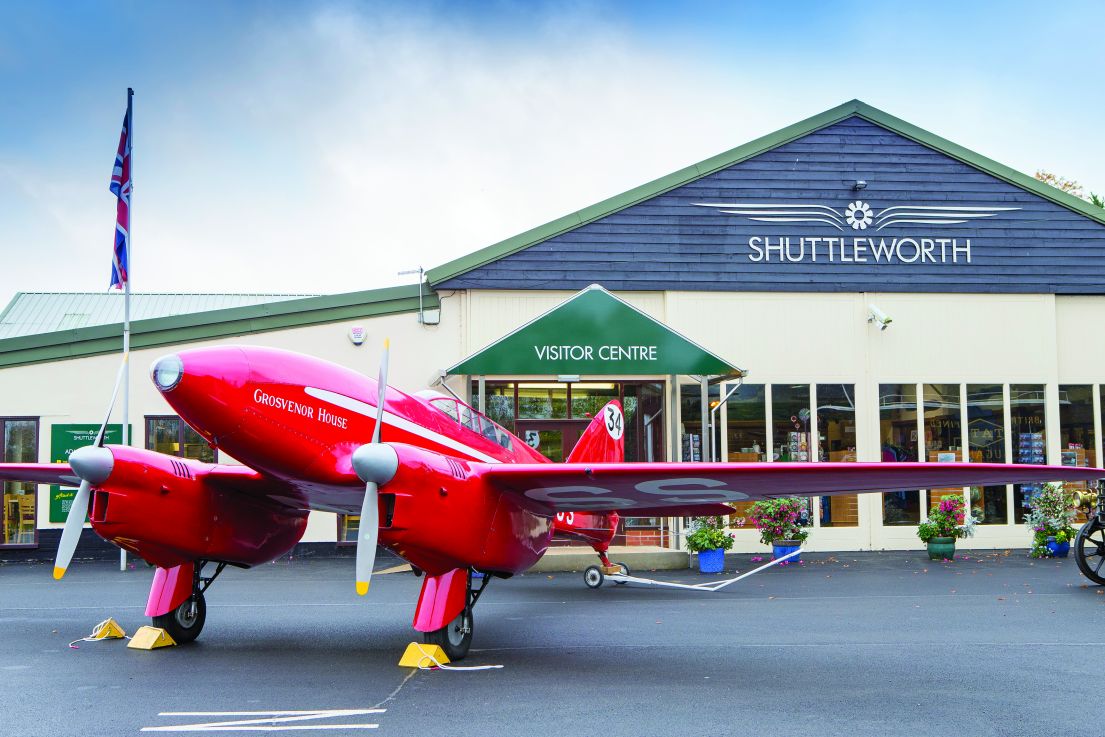 A red plane sat behind blocks in front of the Shuttleworth Visitor Centre building.