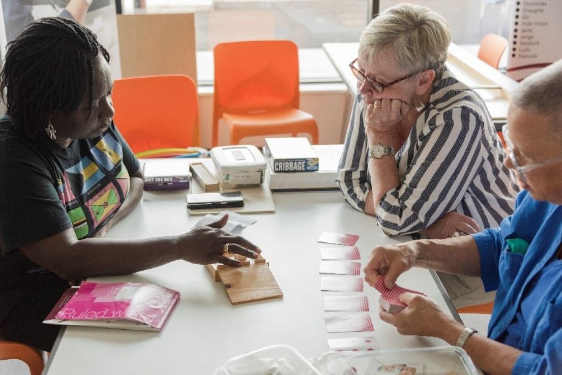 A women showing two other women stat at a table a wooden box Caribbean game.