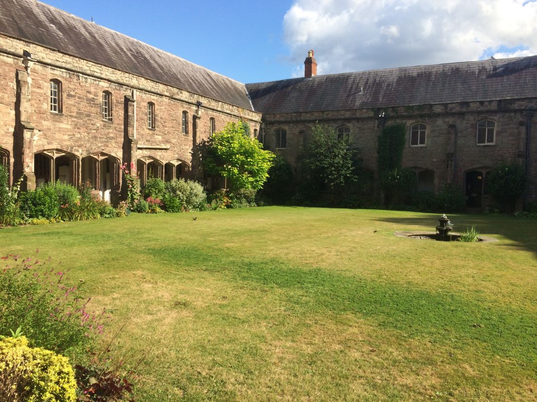 a green grass courtyard in centre of a brown stone bricked cloister at the Cathedral.