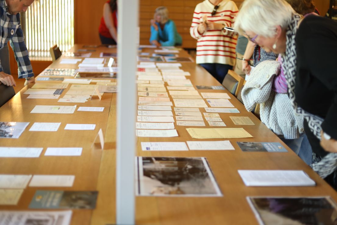 A long wooden table with letters and pictures laid out for the people walking around the table to examine.