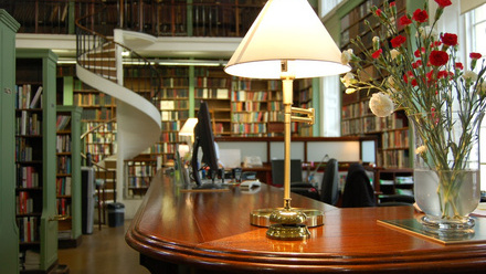 Table lamp and red flowers on a highly polished reception desk in a library.