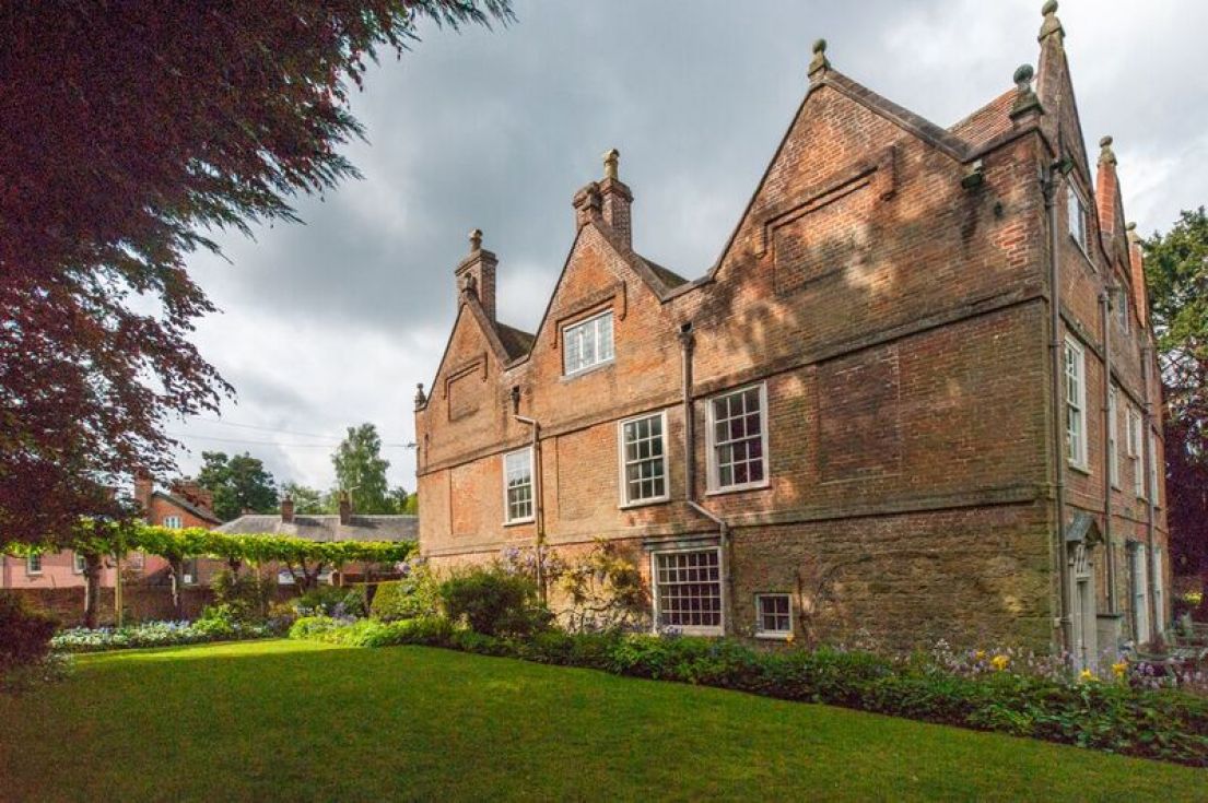 A red brick three story historic property surrounded by a garden.