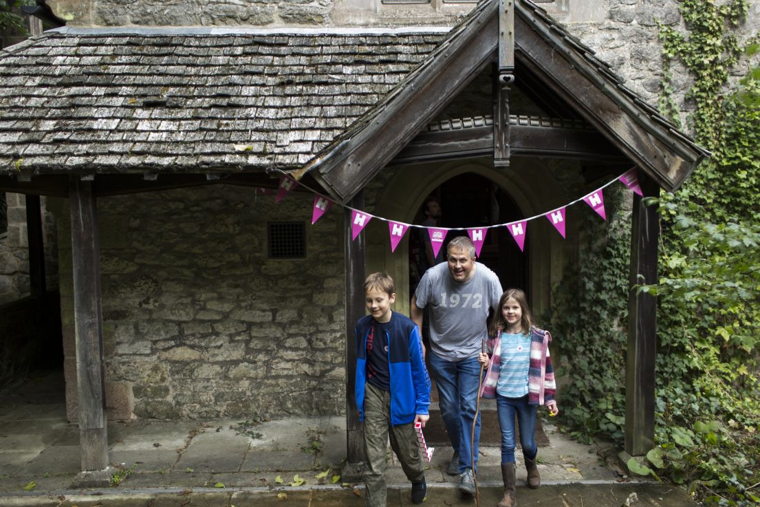 A family with one adult male and two small children excitingly walking out from a church porch adorned in HODs bunting.