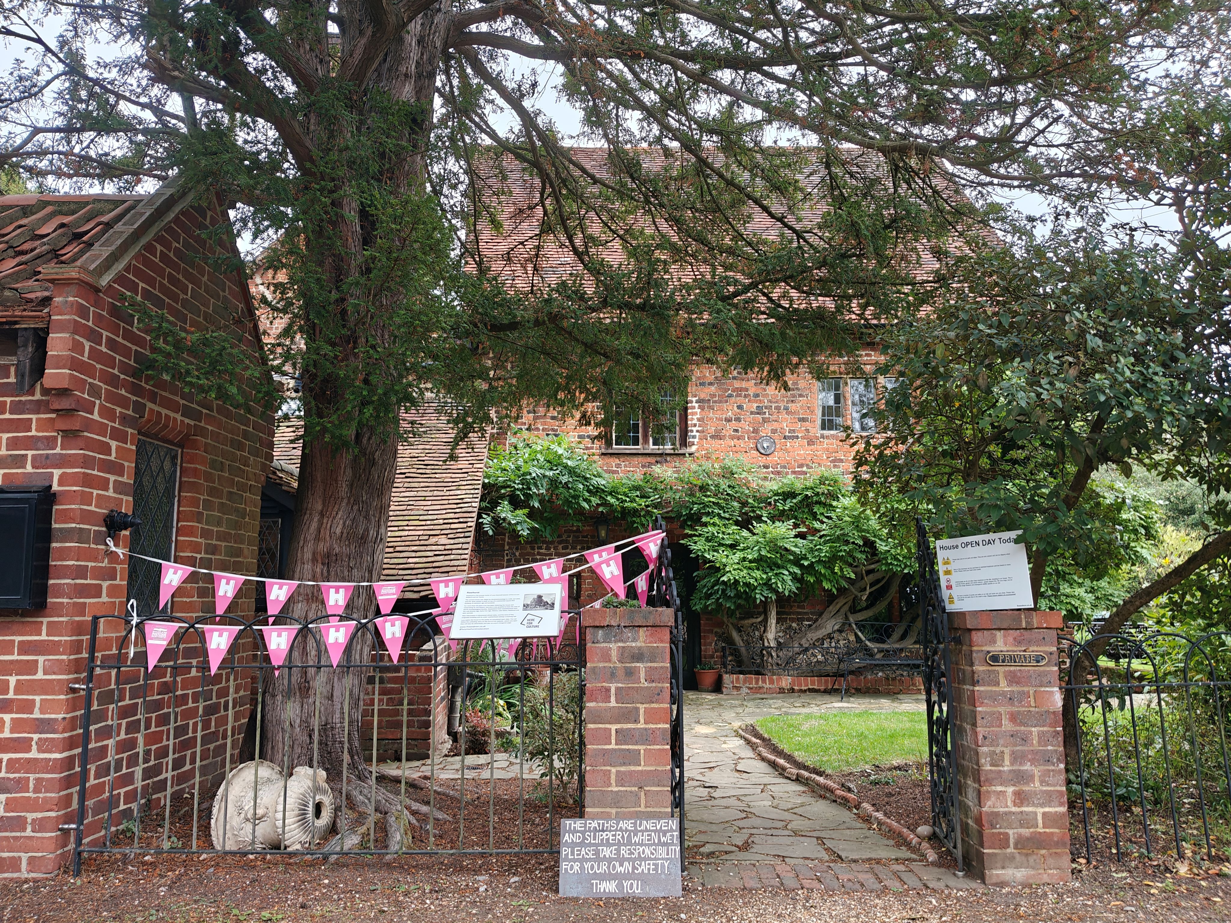 Pink bunting atop railing by a brick gatepost with a path leading to a brick house behind. 