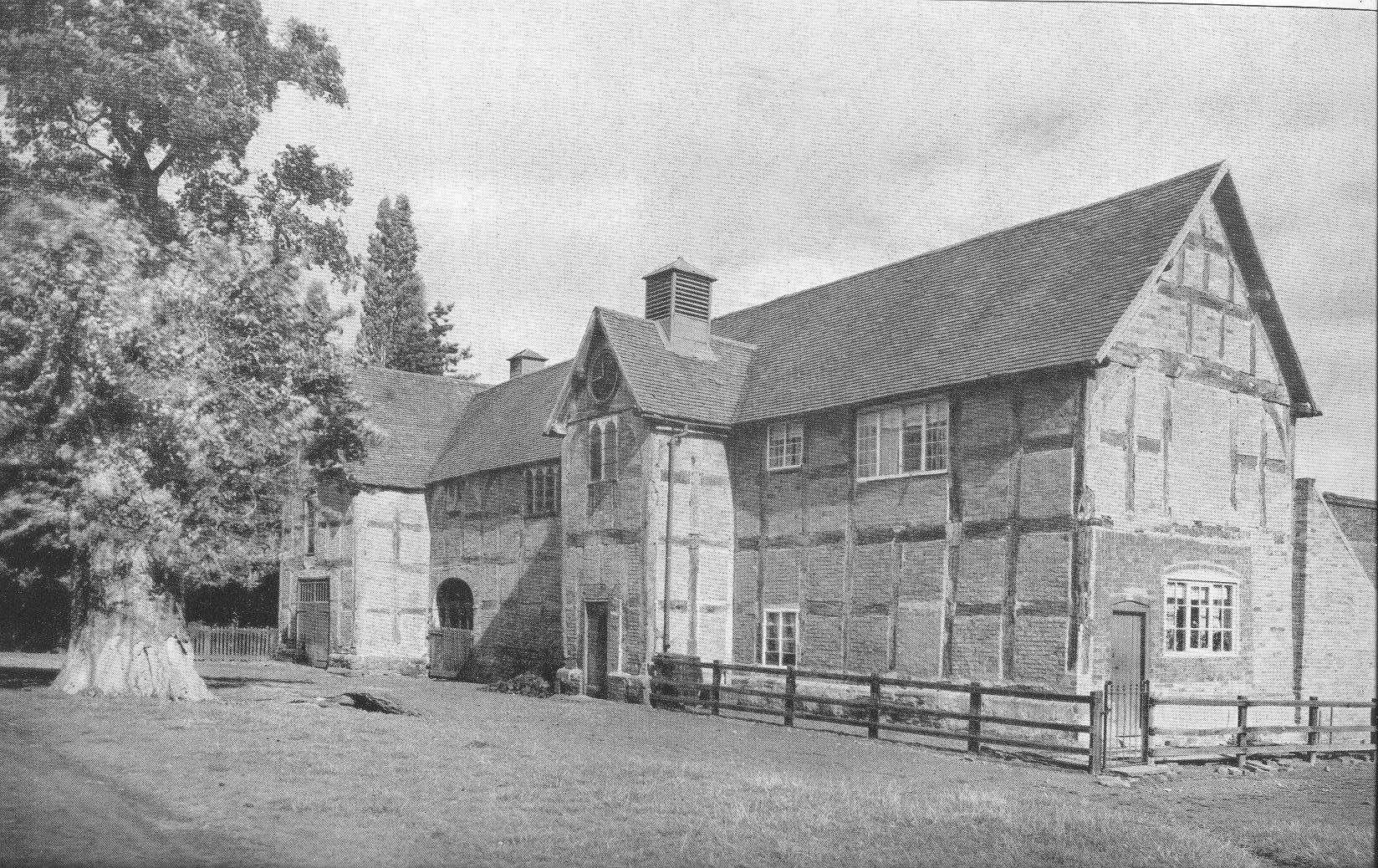 Large two storey timber framed barn with a large tree close by one entrance. 
