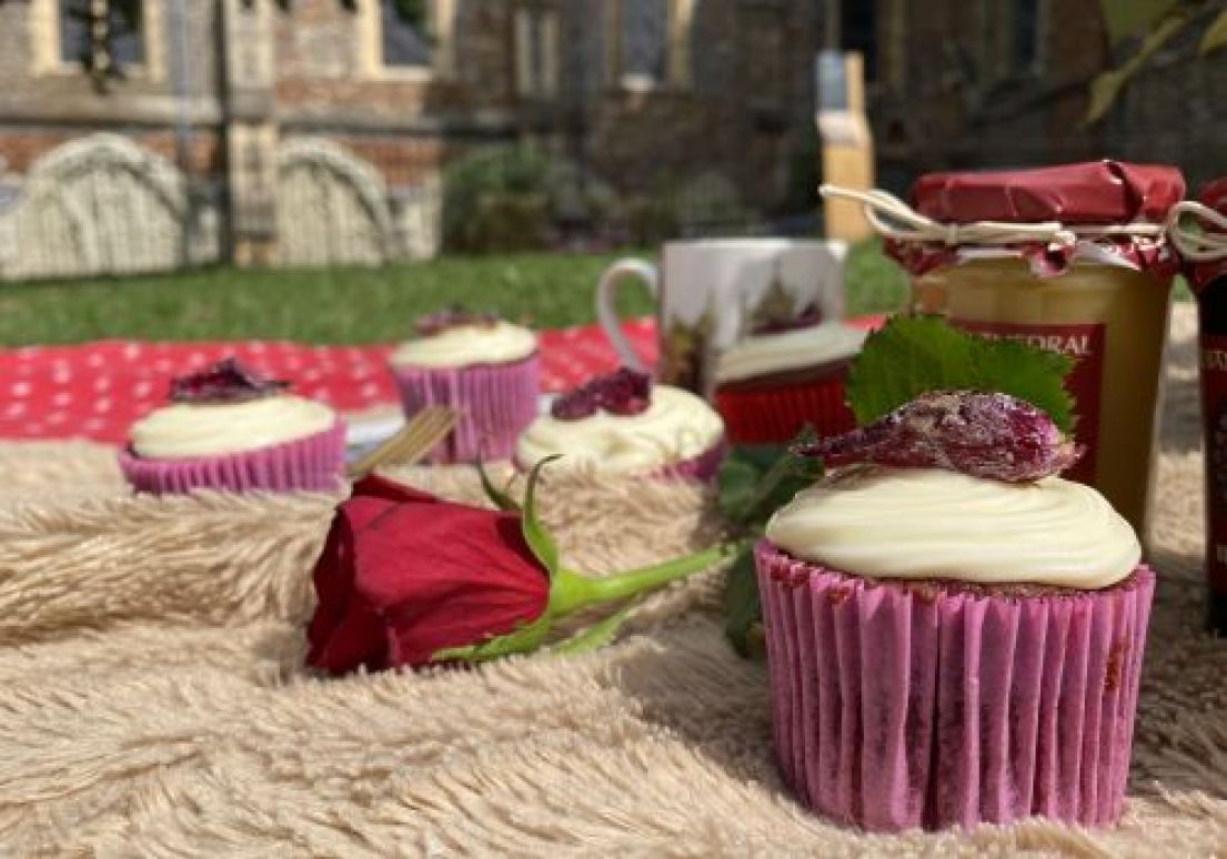 A cupcake picnic on a brown fur and red and white spotted picnic blanket in the grounds of a cathedral garden.