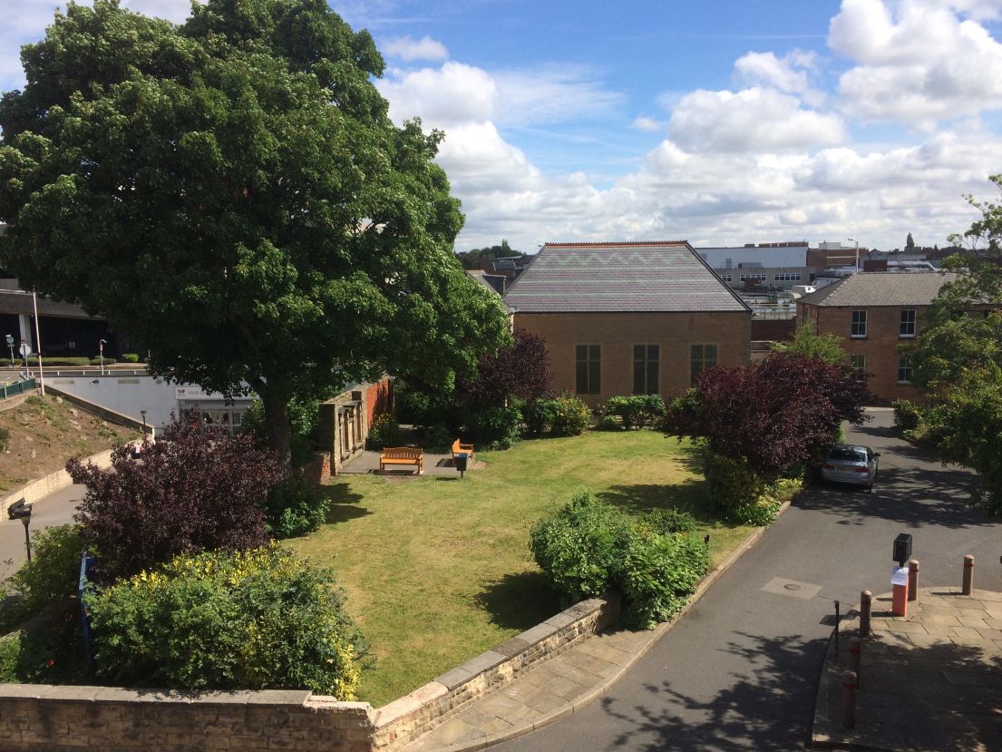 A drone taken picture showing the site of the Unitarian chapel - the one story building overlooked by tall bushy trees.