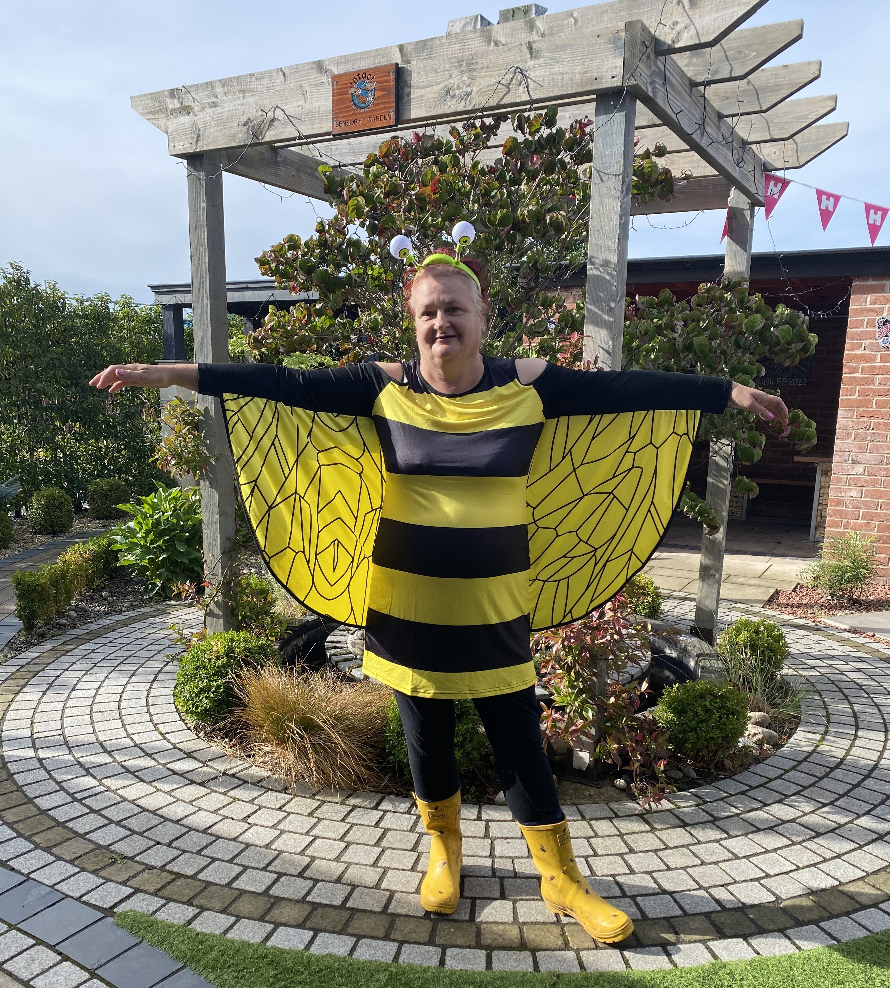 Volunteer in bee costume stood in front of a pergola.