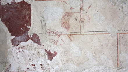 Traces of a drawing that remaining on a wall, a face wearing a crown suggests it was once a king.